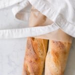 two loaves of sourdough baguettes in a linen bag on a white countertop