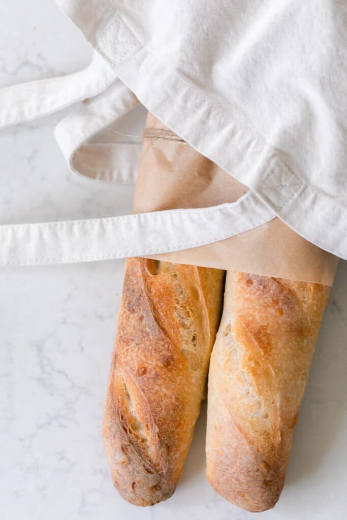 two loaves of sourdough baguettes in a linen bag on a white countertop