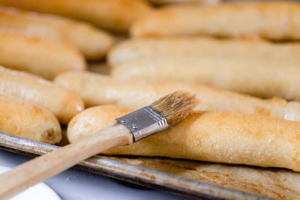 A pan of sourdough breadsticks on a baking sheet fresh out of the oven with a pastry brush on top