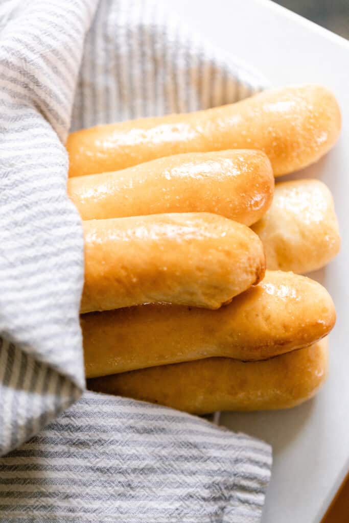 six sourdough breadsticks wrapped in a white and gray towel