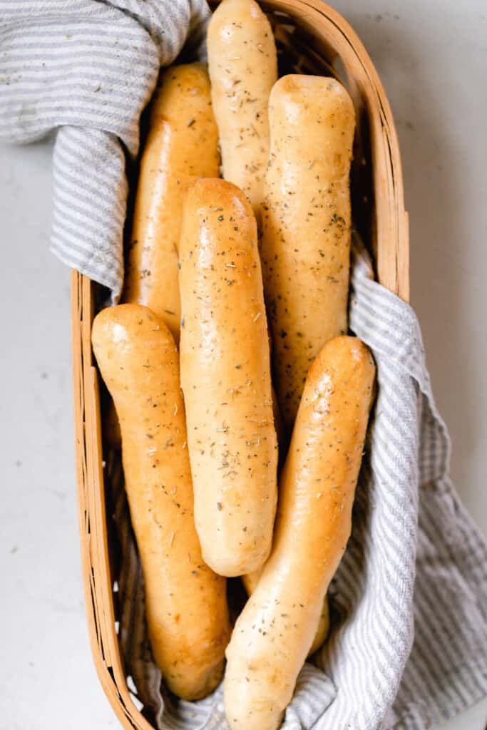 overhead photo of a long basket lined with a gray and white stripped towel full of sourdough bread sticks