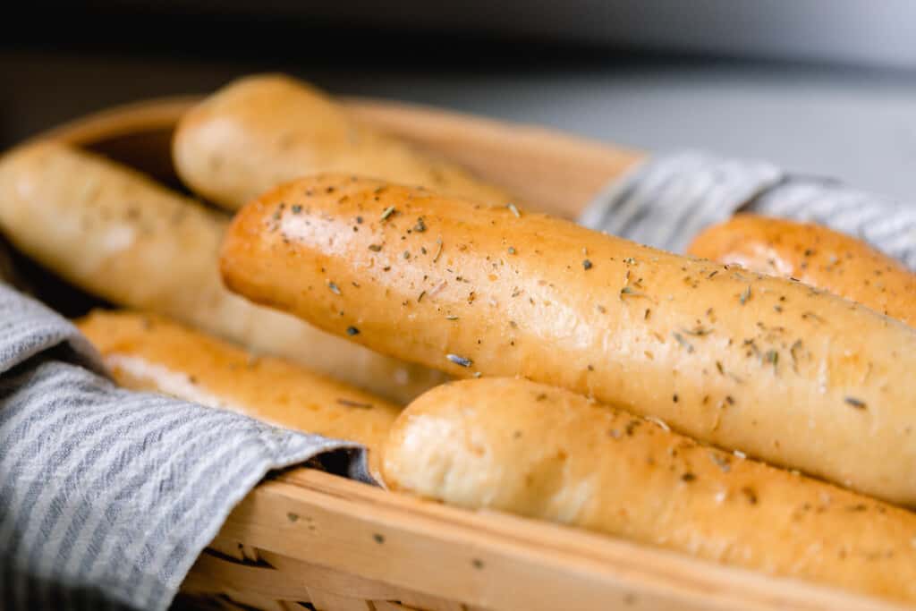 a towel lined basket full of sourdough bread sticks topped with a herb garlic butter