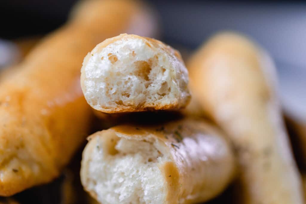 close up of sourdough breadsticks with. one cut in half to show the airy interior