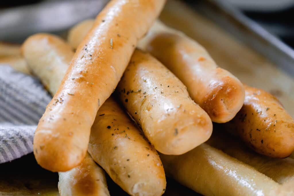 sourdough breadsticks piled on top of each other on a pan with a blue and white striped tea towel to the side