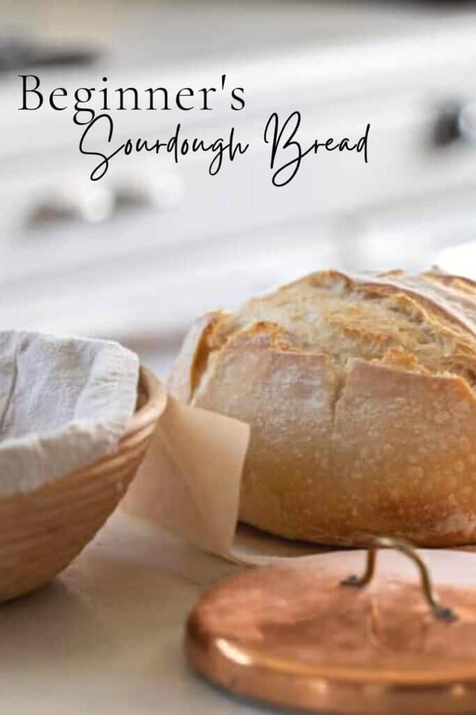 loaf of sourdough bread on parchment paper a counter with a copper lid in front of the loaf and a banneton basket to the left