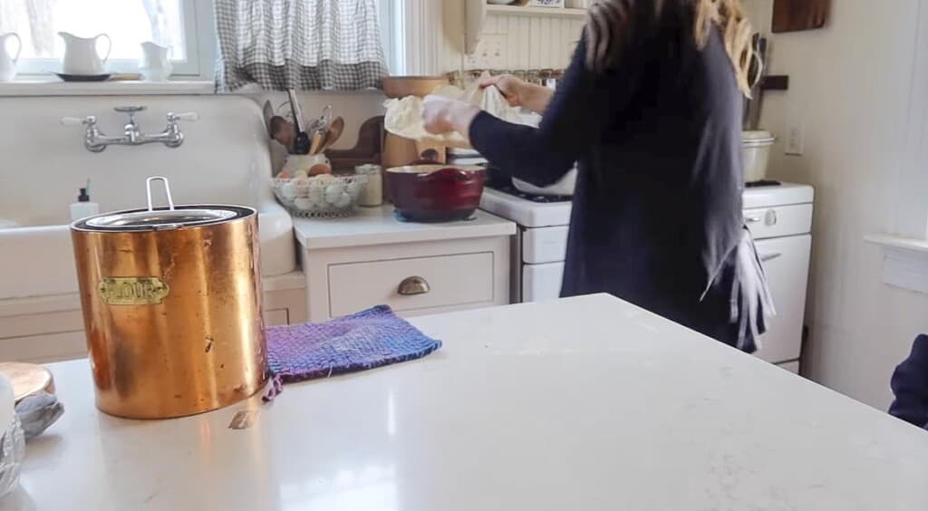 a woman transferring bread dough on parchment paper into a hot dutch oven