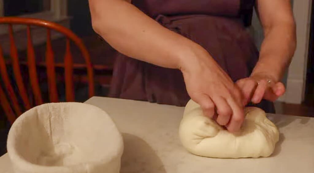 shaping a loaf of sourdough bread on a white countertop