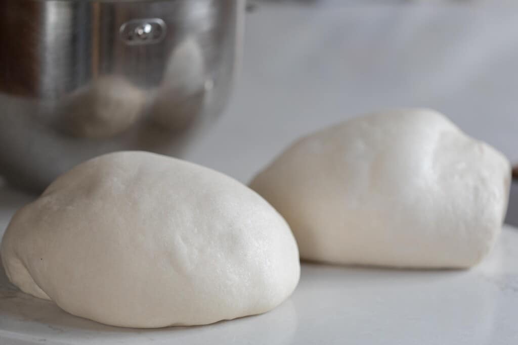 Two balls of potato flake sourdough starter sandwich bread on a white counter top with a stainless steel mixer bowl in the background