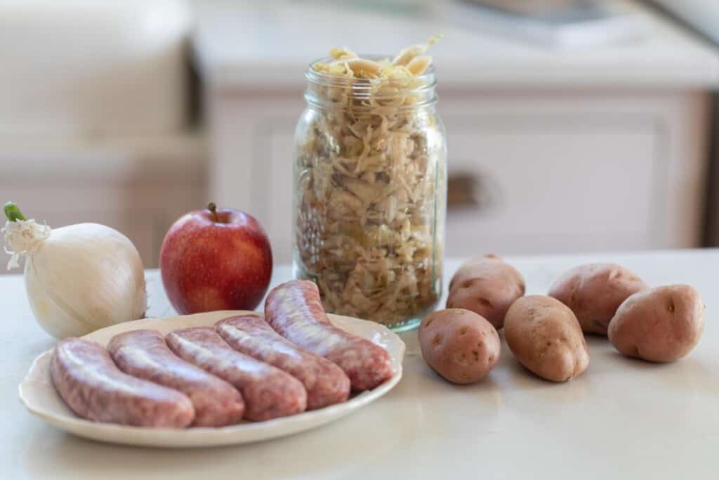 Ingredients for sausage and sauerkraut skillet dinner including onions, potatoes, apple, sauerkraut and smoked sausages