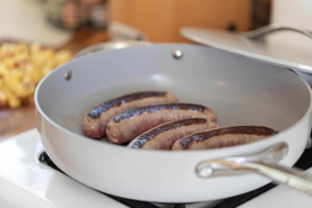 Four bratwursts cooking in a gray large skillet on a white stove