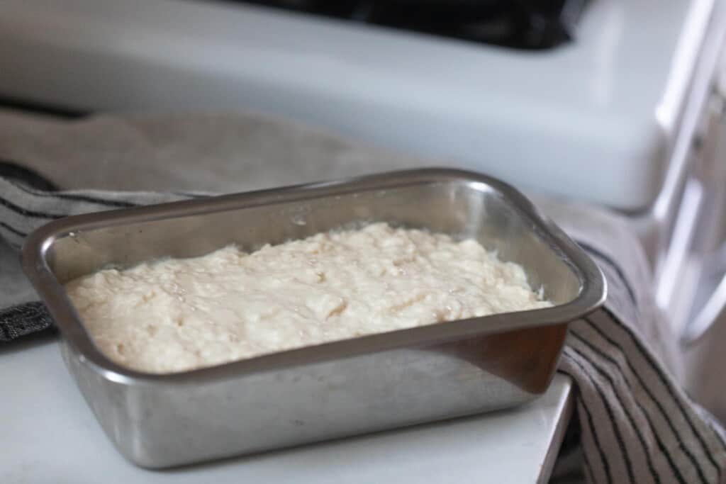 Sourdough beer bread in a stainless steel loaf pan sitting on a white counter before going into the oven