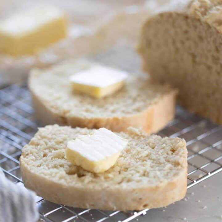 A loaf of sourdough beer bread cut with two slices with a tab of butter on each sitting on a wire rack