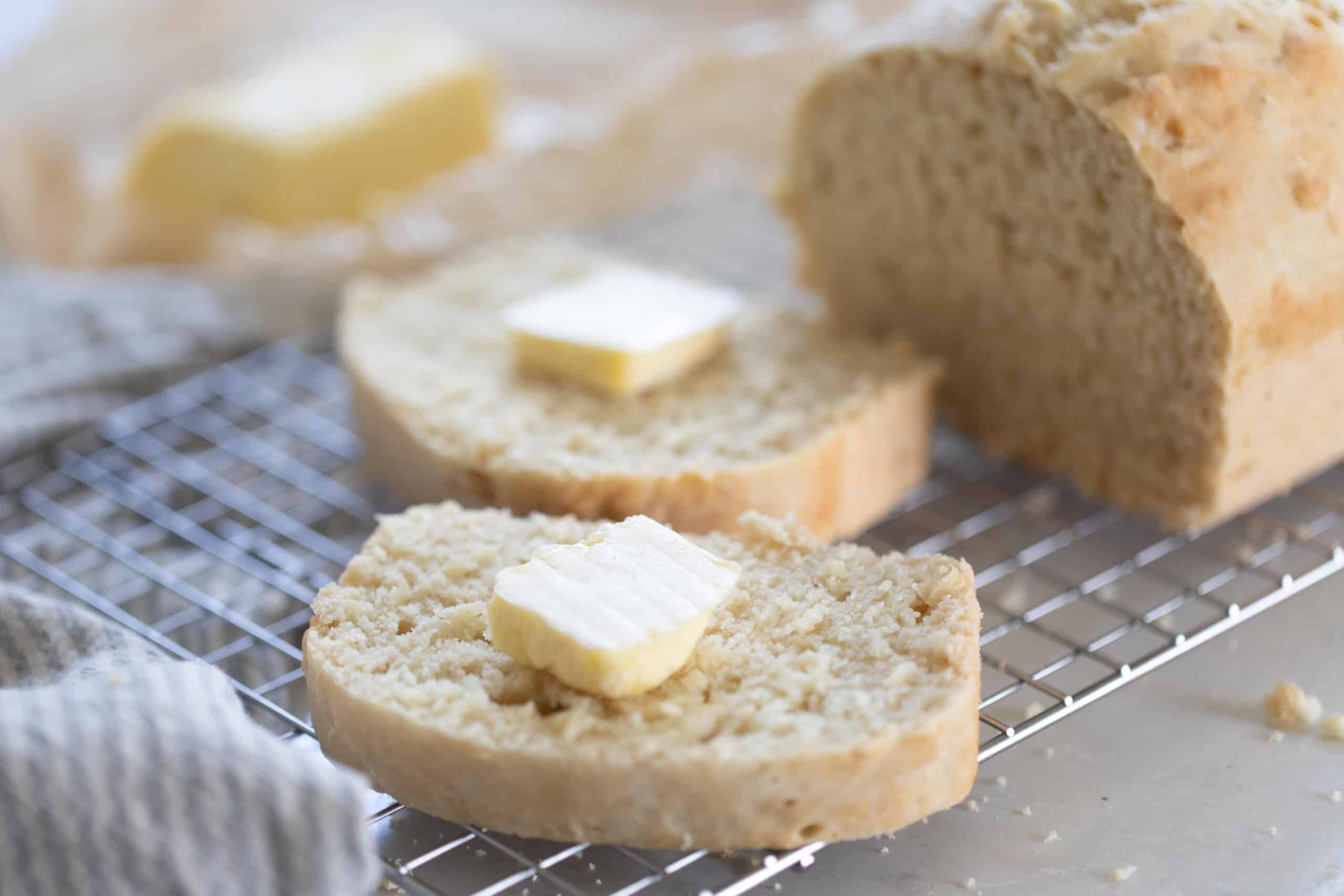 A loaf of sourdough beer bread cut with two slices with a tab of butter on each sitting on a wire rack
