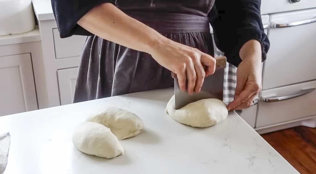 woman in a blue apron cutting dough with a bench scraper on a white quartz countertop