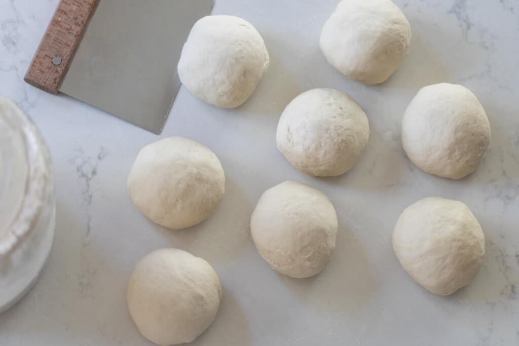 dough balls on a white countertop with a bench scraper to the left