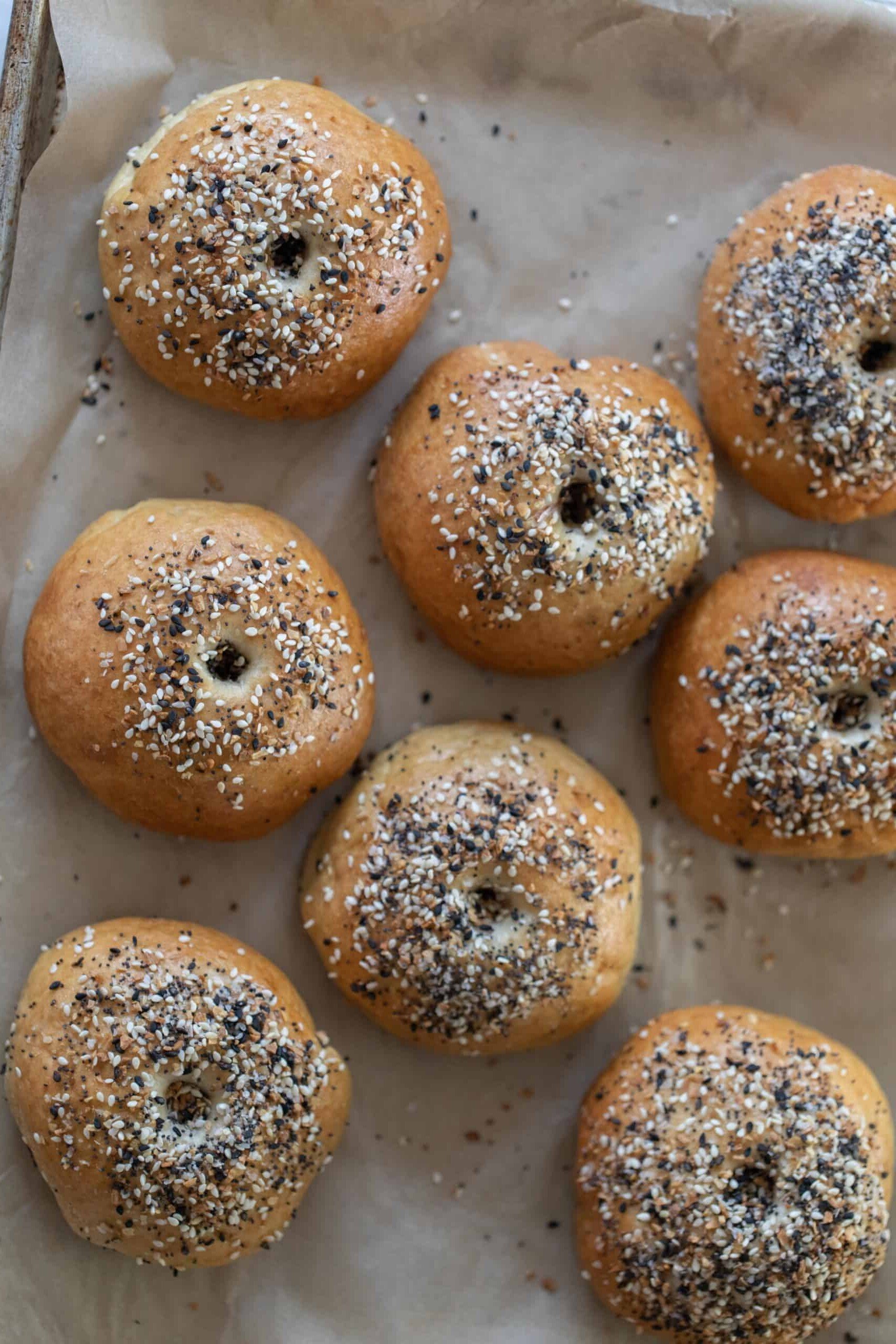 overhead photo of sourdough discard bagels topped with everything seasoning on a parchment lined baking sheet