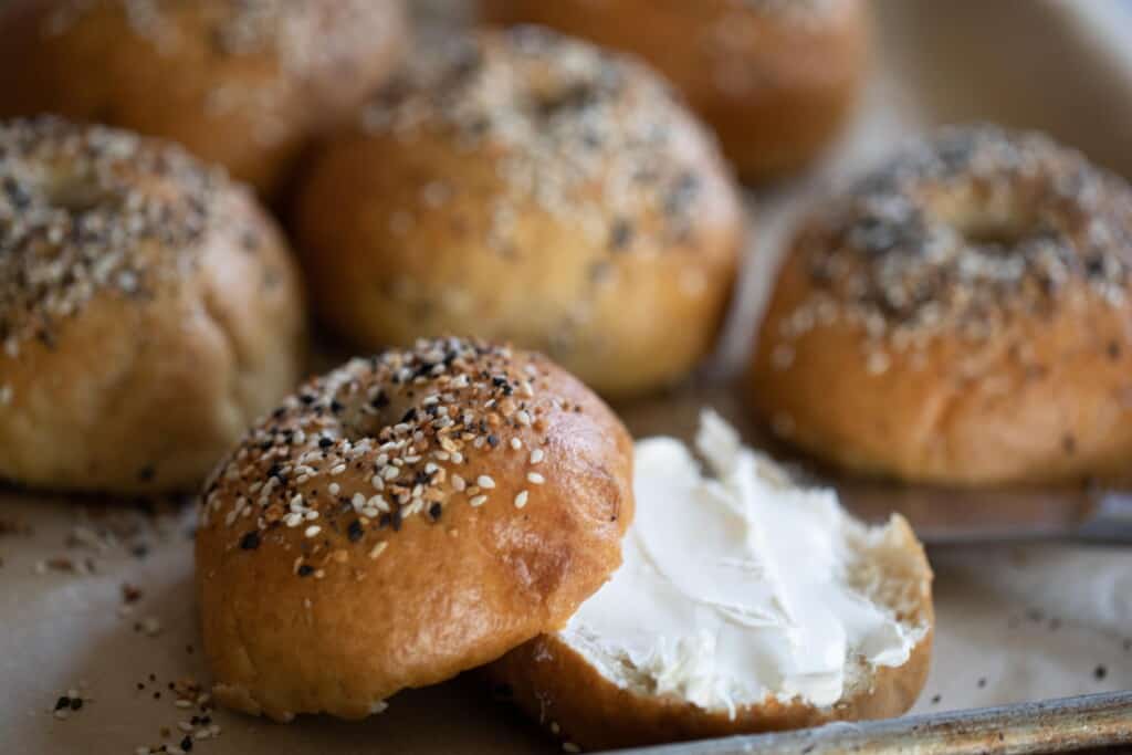 sourdough bagel sliced in half and covered with cream cheese, More bagels are in the background