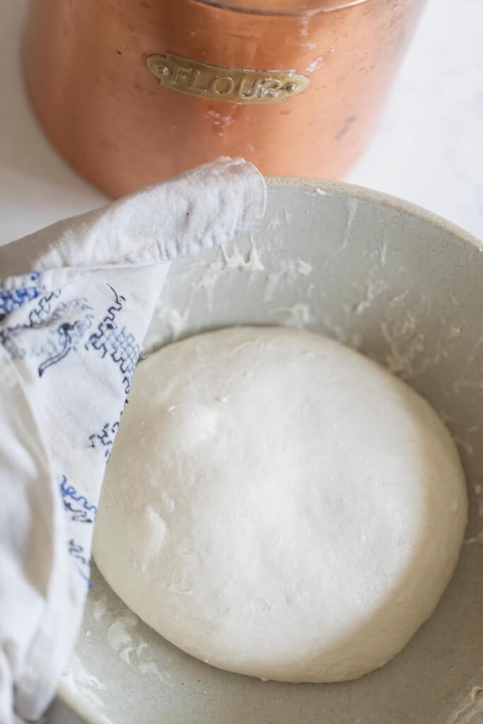 beginners sourdough bread dough after rising until doubled in a stone bowl with a blue and white towel on the edge of the bowl