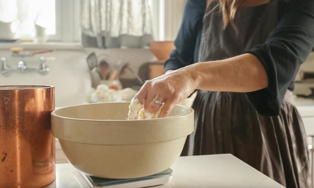 women mixing up ingredients in a large mixing bowl in a white kitchen