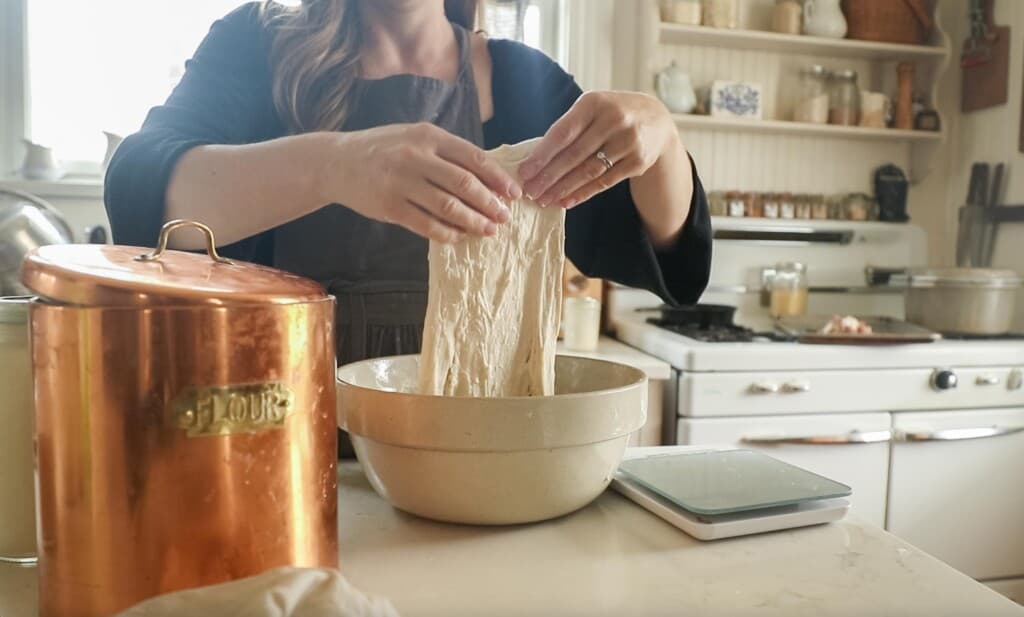 a women pulling dough up dough from a large bowl to complete a stretch and fold for making sourdough bread