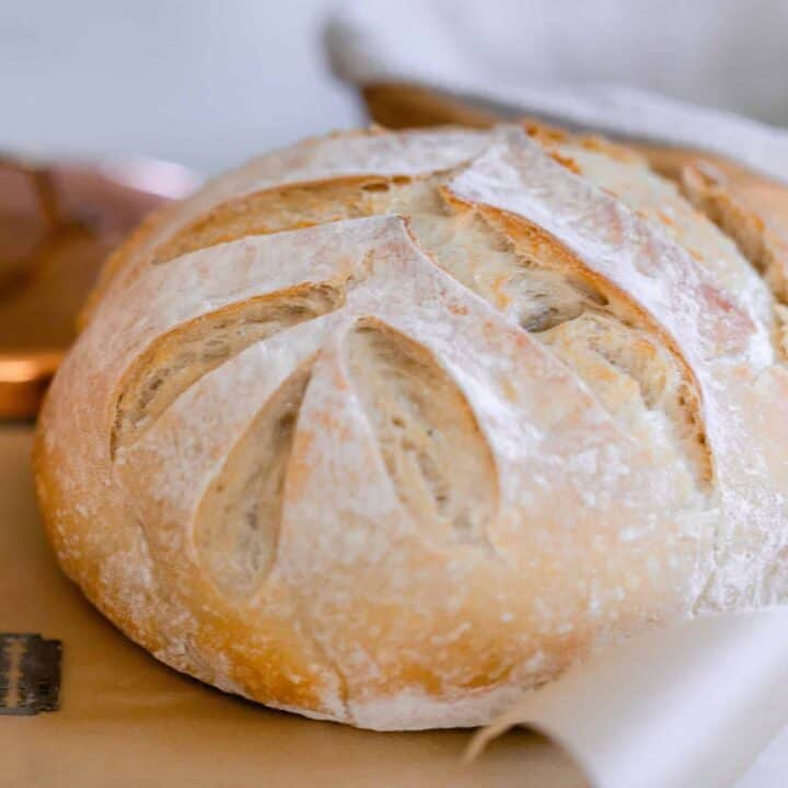 sourdough bread with a leaf pattern on parchment paper with a copper container to the left