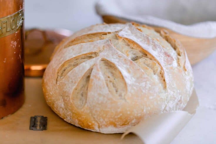 sourdough bread with a leaf pattern on parchment paper with a copper container to the left