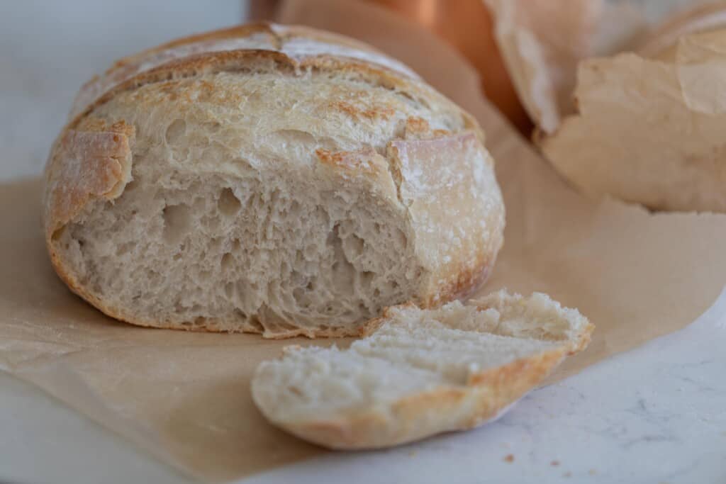 Sourdough loaf with one piece sliced on a piece of brown parchment paper