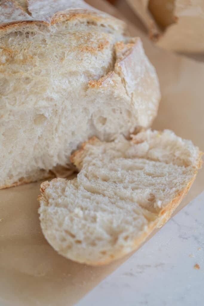 a loaf of sourdough bread with a slice laying next to the loaf on parchment paper