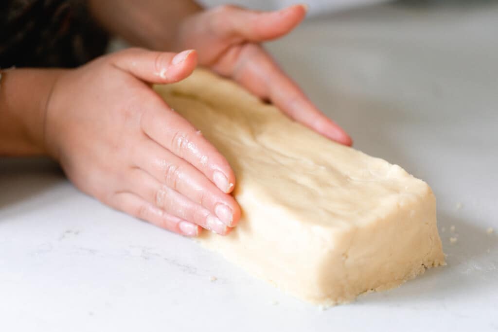 two hands shaping the sourdough shortbread cookies into a brick shape on a white counter top