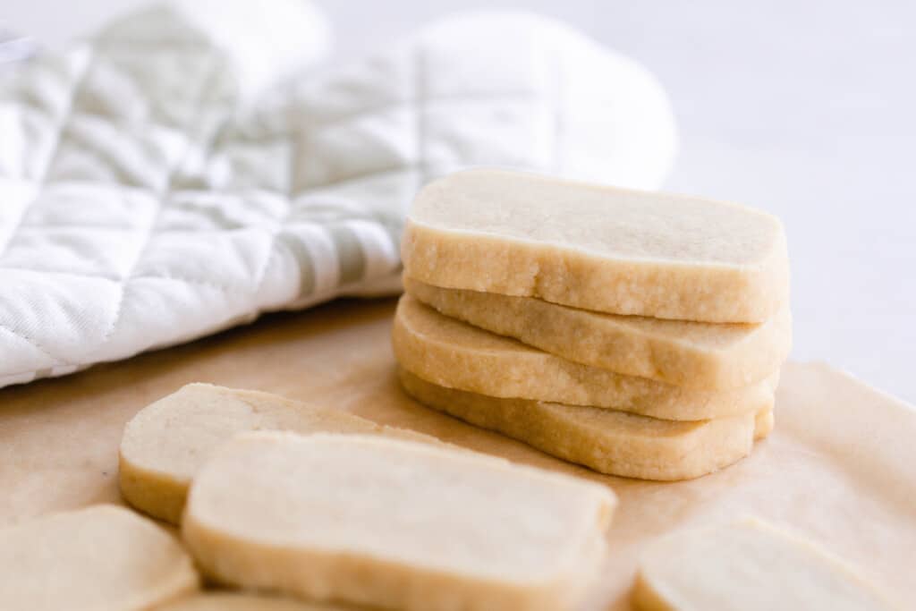 sourdough shortbread cookies stacked up on a wooden cutting board with a white oven mitt in the background