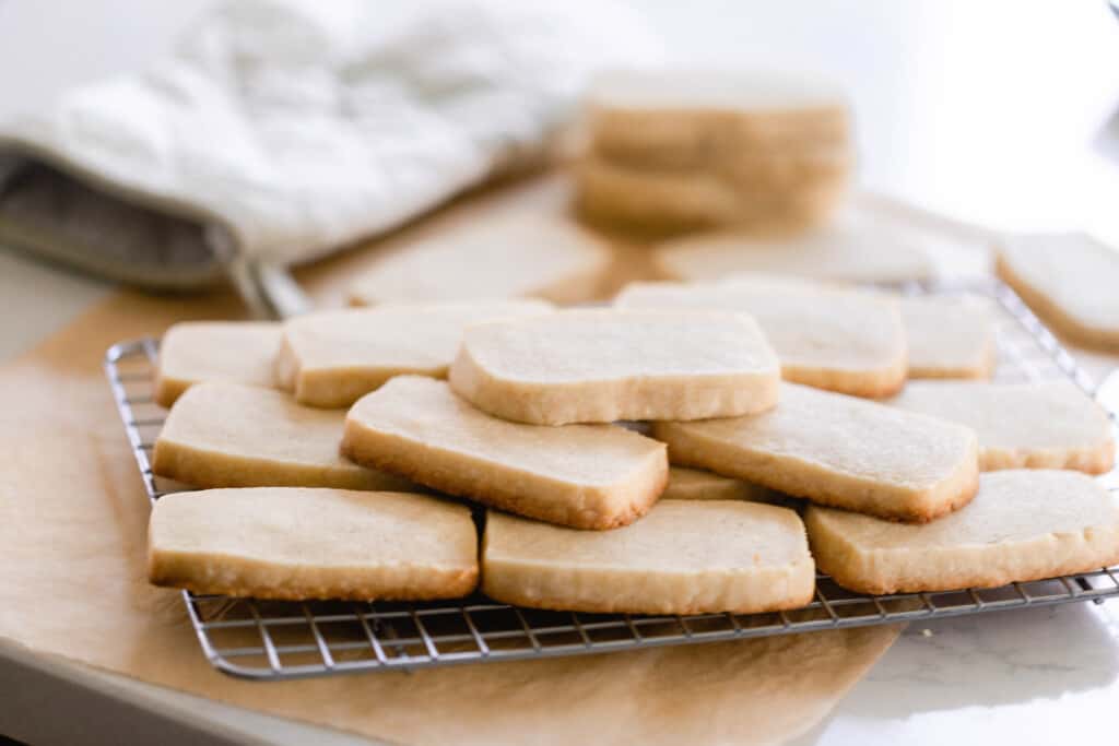 sourdough shortbread cookies stacked on top of each other on a wire cooling wrack that is sitting on a wooden cutting board