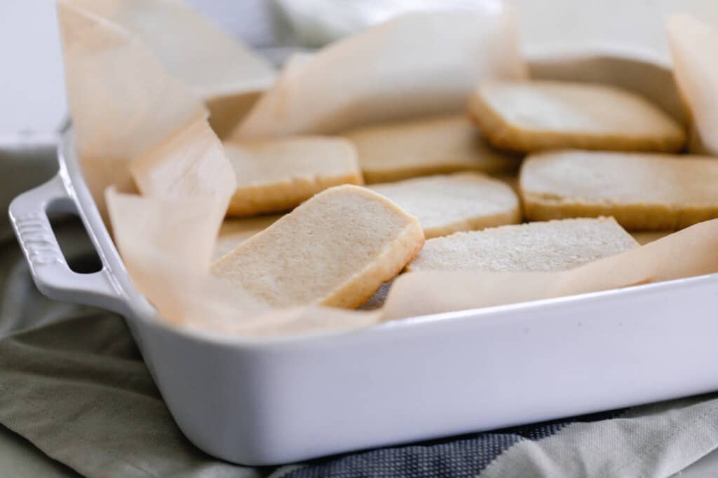 sourdough shortbread cookies stacked in a white casserole dish lined with parchment paper