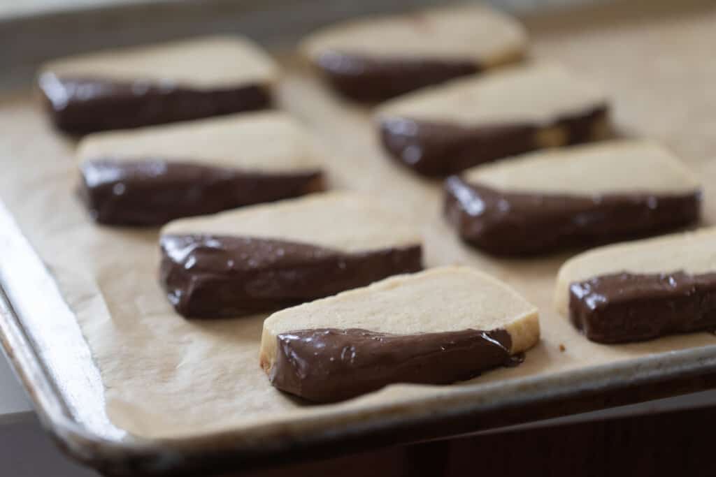 sourdough shortbread cookies with the corners dipped in chocolate all sitting on a parchment paper lined baking sheet