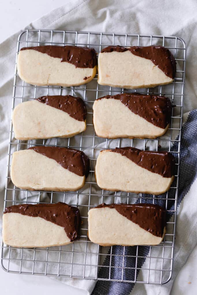 eight sourdough shortbread cookies with the corners dipped in chocolate sitting on a cooling rack on the counter