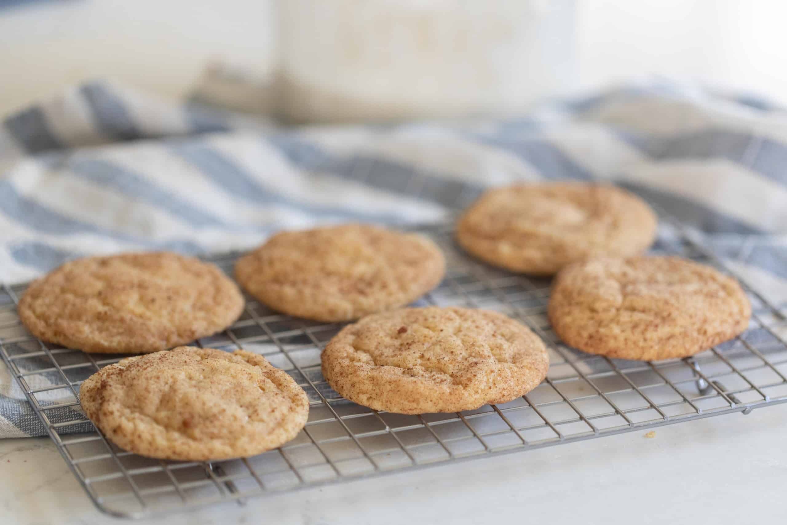 six sourdough snickerdoodle cookies on a wire cooling rack over a blue and white stripped towel