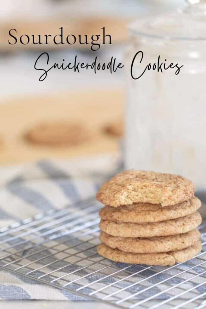 five sourdough snickerdoodle cookies stacked up on a wire rack over a white and blue stripped towel with a glass of milk behind the stack of cookies