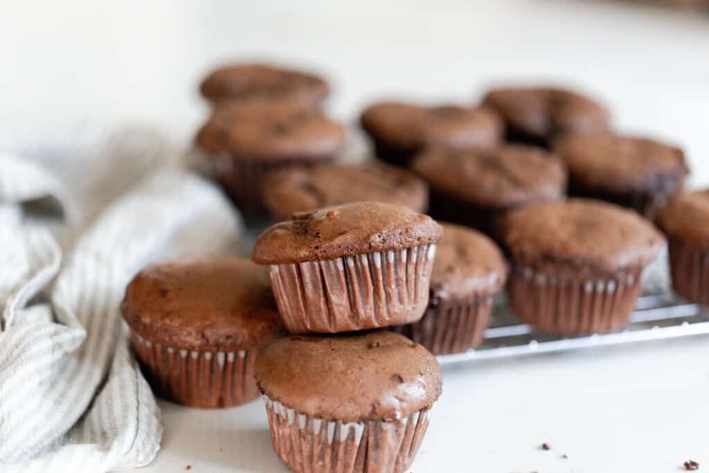 A stack of einkorn protein muffins on a cooling rack on a white counter with a white tea towel