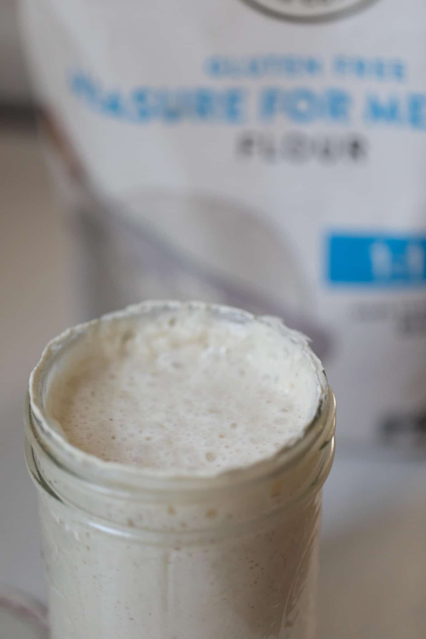 a major full full of sourdough starter made with gluten free flour. A bag of gluten free 1 for 1 flour is in the background
