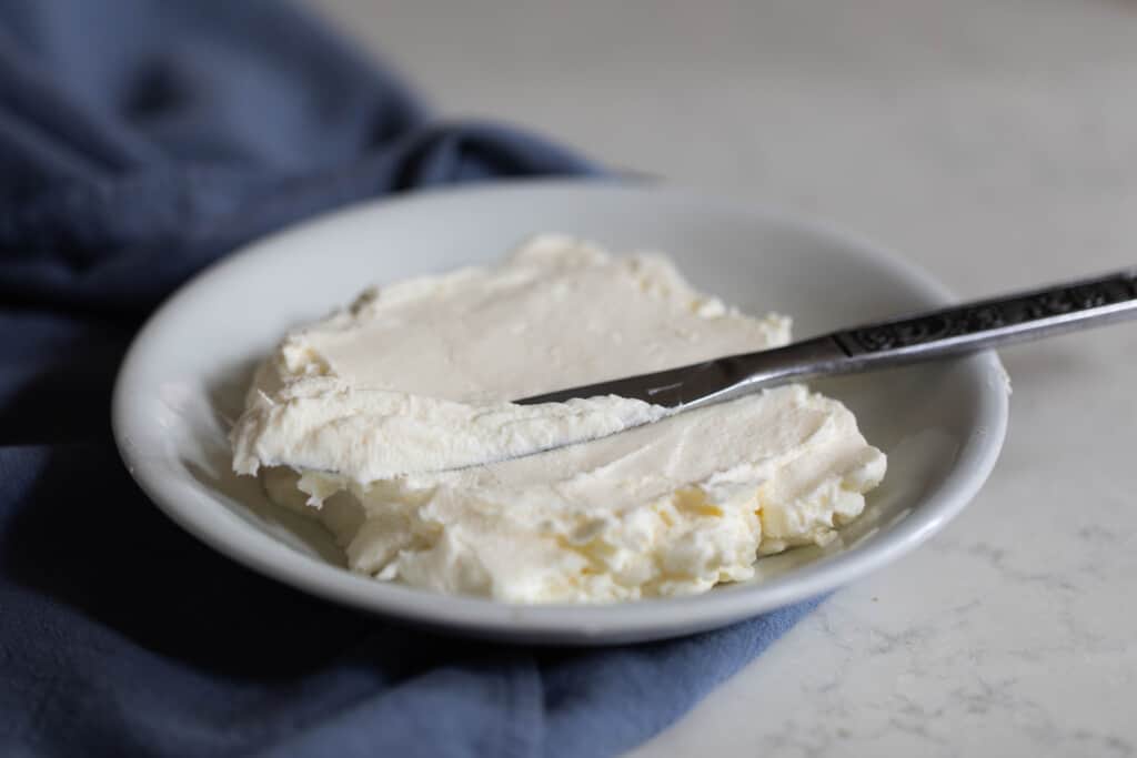 Greek yogurt cream cheese in a white dish on a blue towel with a silver knife