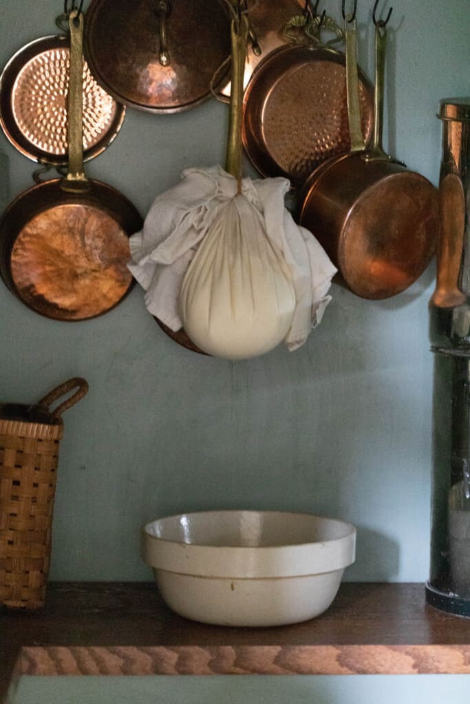 Greek yogurt cream cheese hanging in a pantry to dry with copper pots int eh background