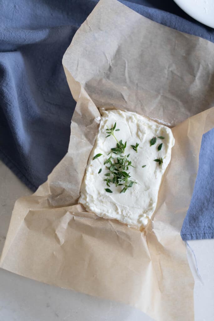 A block of greek yogurt cream cheese with herbs on top sitting on parchment paper that is on a blue towel