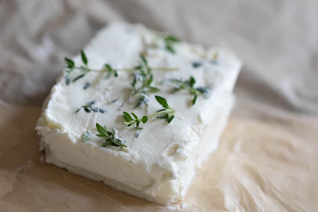 A square block of Greek yogurt cream cheese with herbs on top on a piece of parchment paper