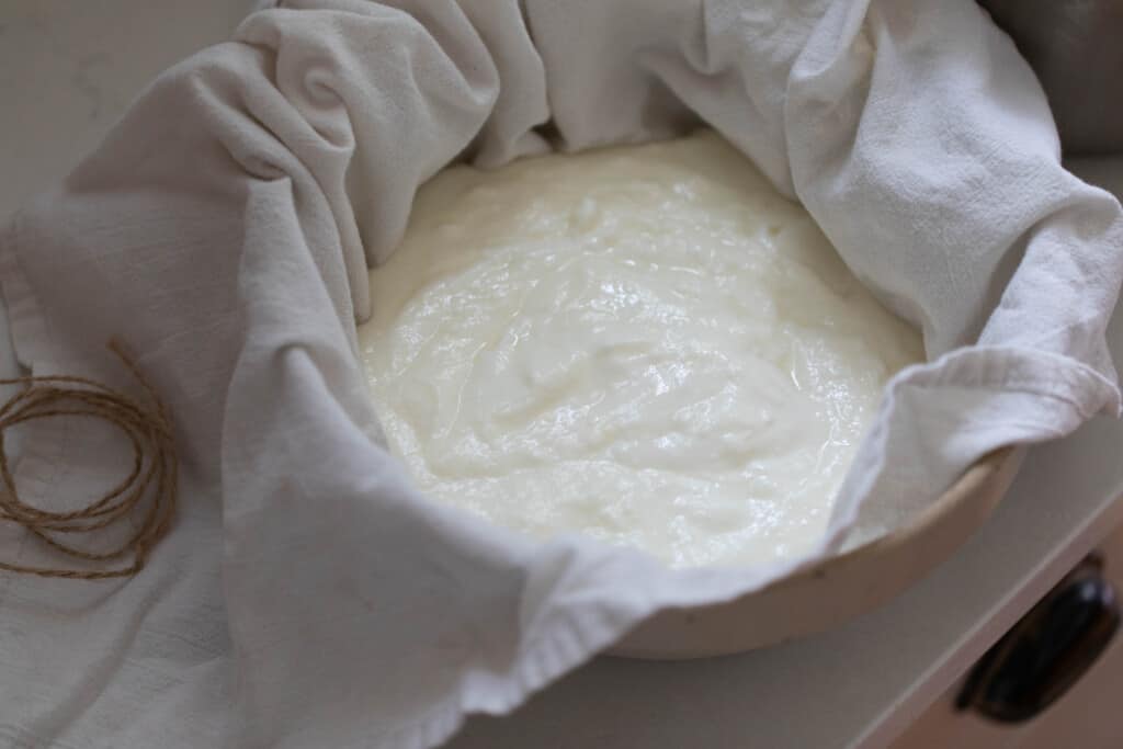 Greek yogurt in a towel over a colander and large bowl