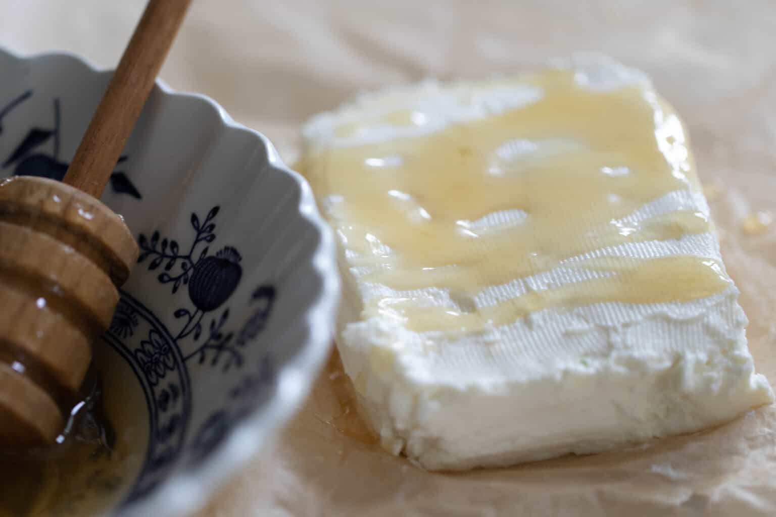 A block of Greek yogurt cream cheese with honey drizzled on top with a bowl of honey on the side