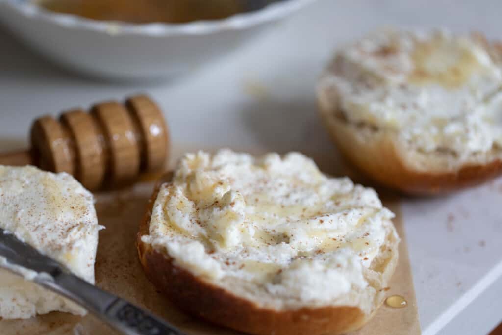 Two slices of bread slathered with greek yogurt cream cheese and honey on a white countertop