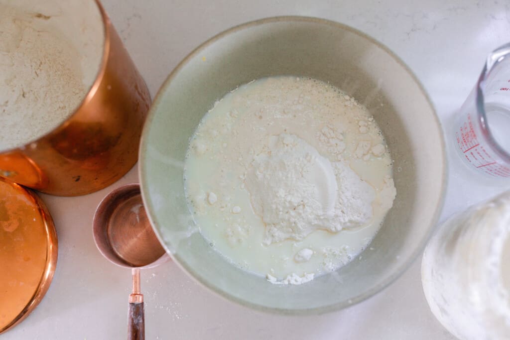 flour water and sourdough starter in a bowl with containers of ingredients surrounding the bowl