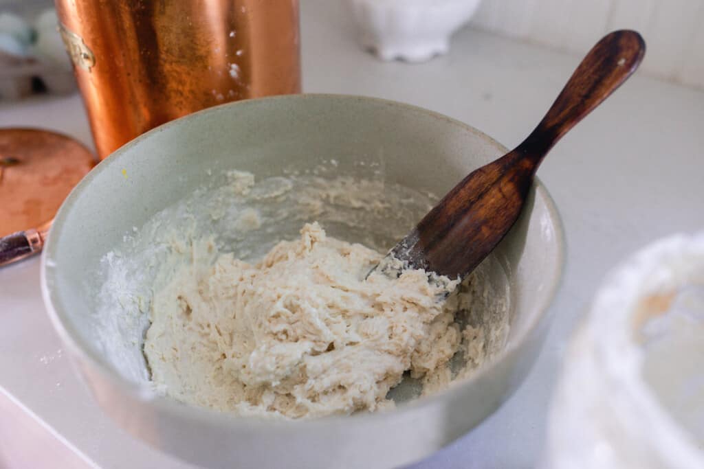 sourdough starter, milk, and flour in a large bowl with a wooden spatula