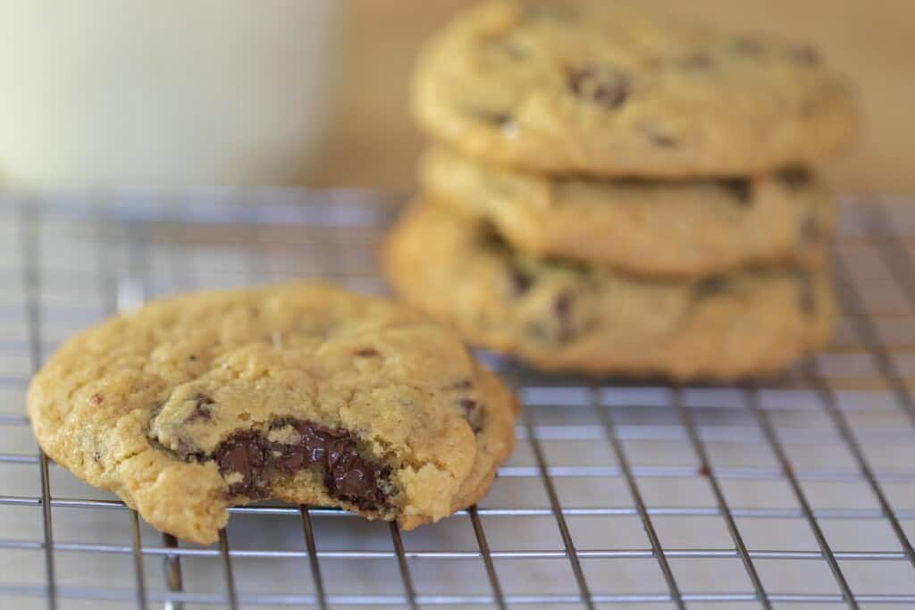 sourdough chocolate chip cookie with a bite out on a wire rack with a stack of three chocolate chip cookies in the background