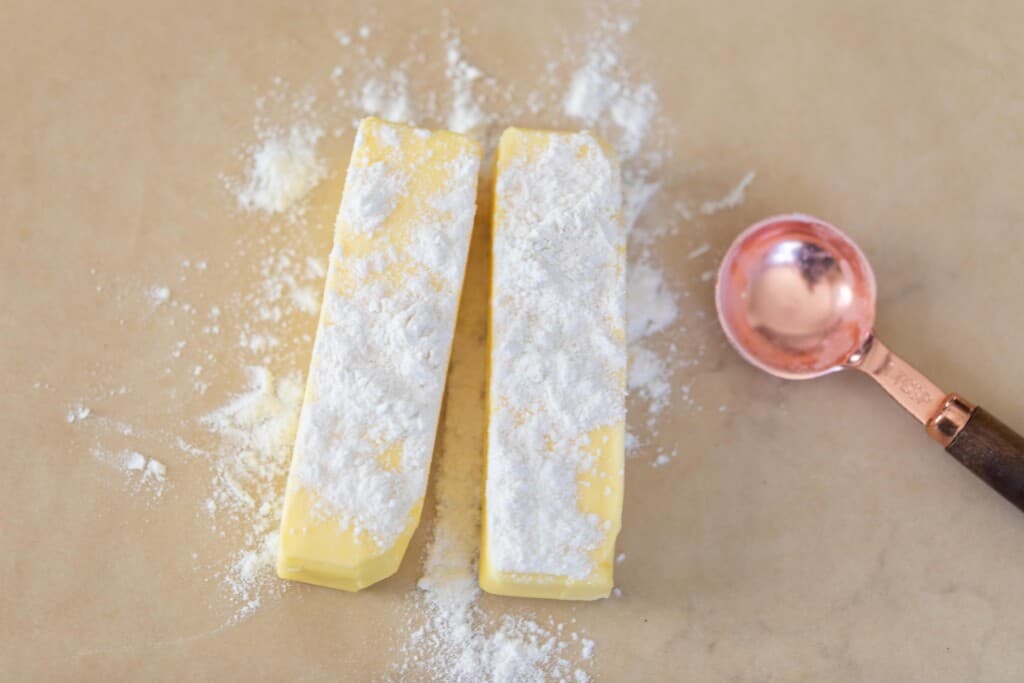 butter sprinkled with flour on parchment paper with a copper measuring spoon to the left