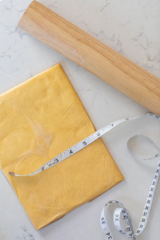 butter rolled out into a 6 by 8" rectangle on a white quartz countertop with a rolling pin to the left and a measuring tape over top of the butter